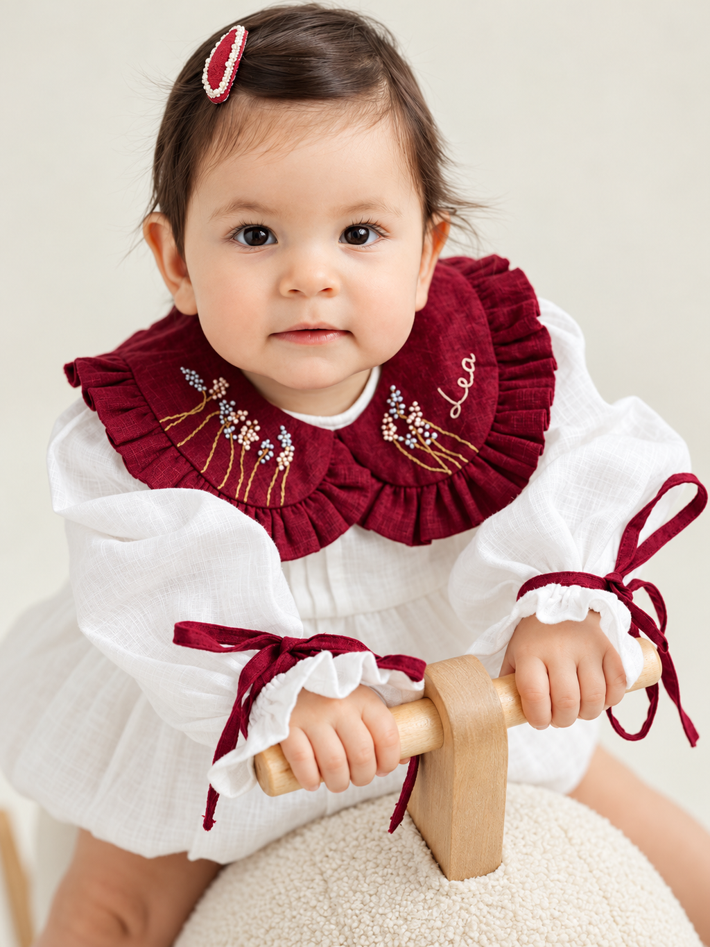 Baby wearing white romper with burgundy embroidery and cuffs