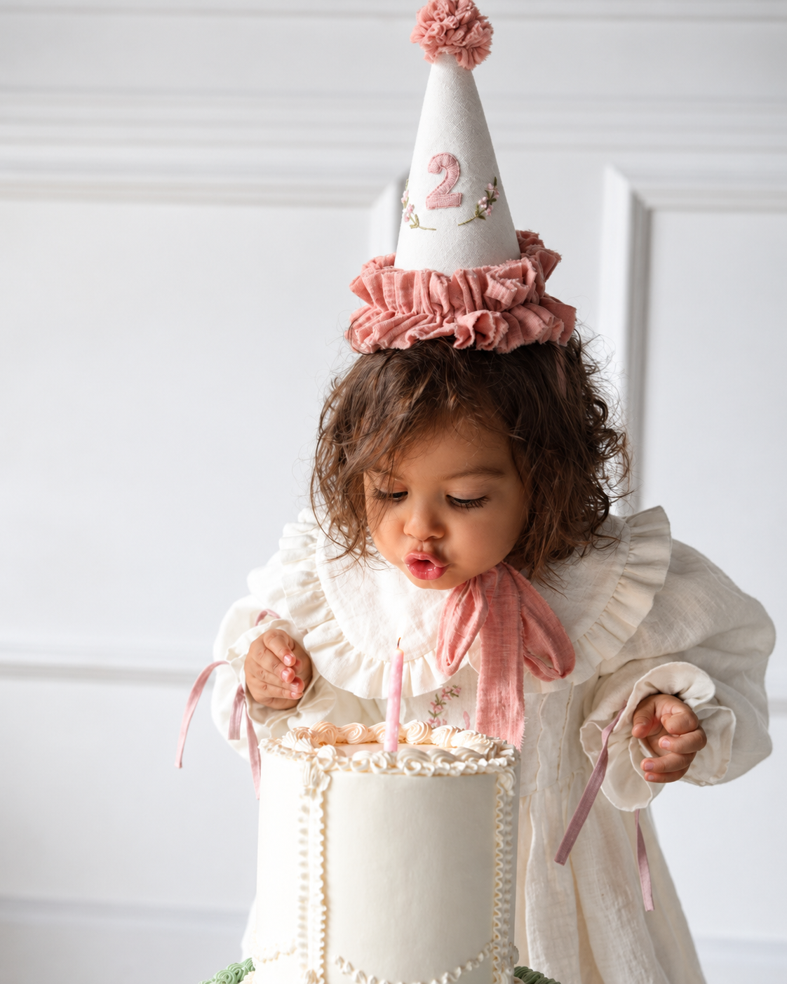 Girl in ivory birthday dress celebrating with candle and birthday hat