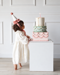 Girl wearing ivory floral embroidered birthday dress next to pastel tiered cake